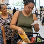 Família brasileira em supermercado ilustrando como funciona o cashback do IBS e da CBS para inscritos no CadÚnico